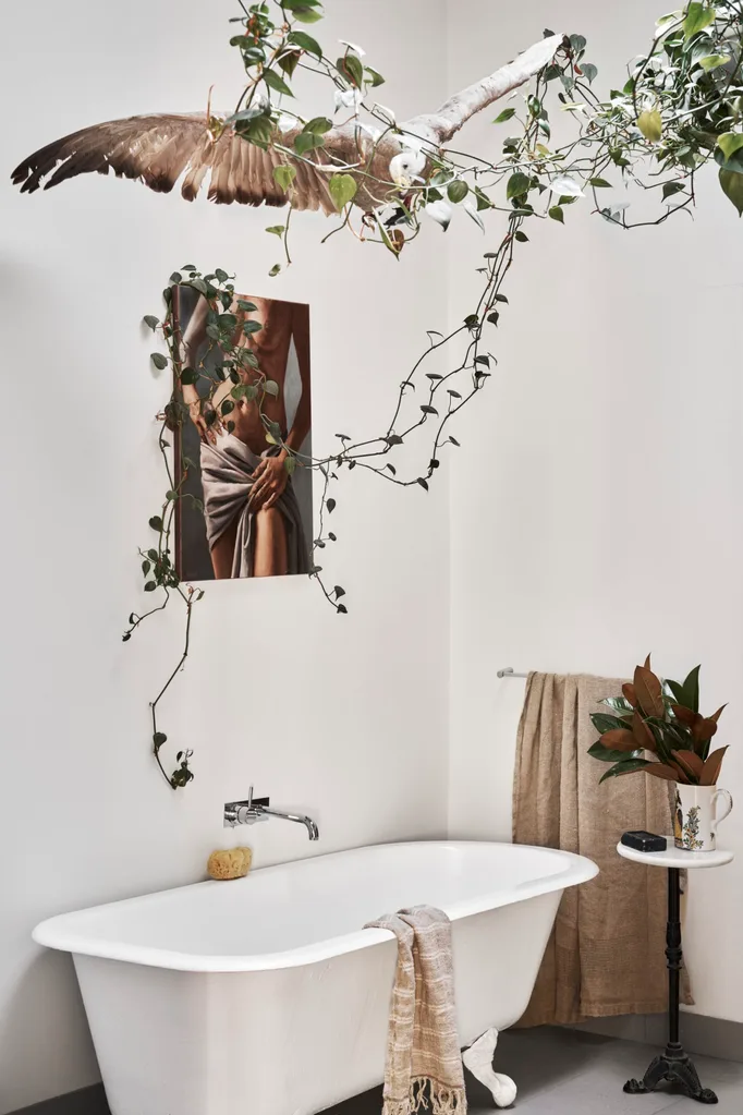 A freestanding bathtub with a taxidermy bird hung above