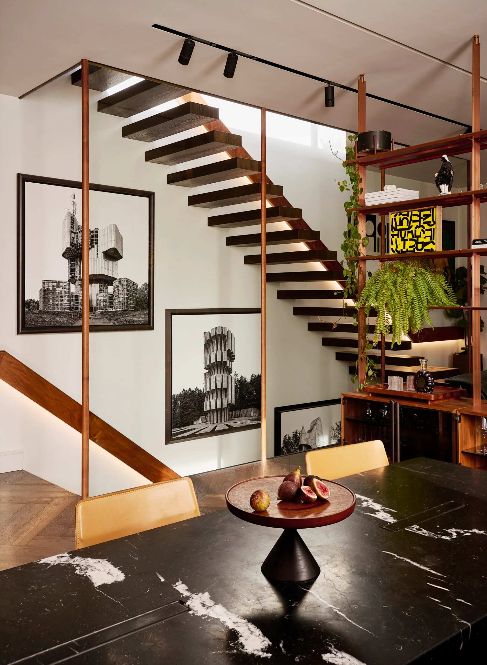 A dining area beside a floating staircase and open timber shelving