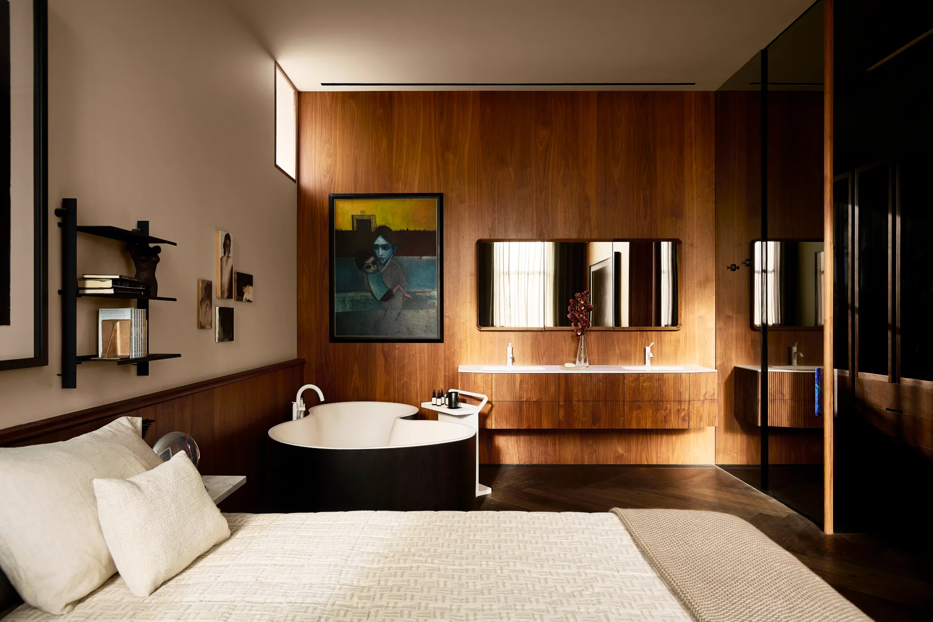 A bedroom with an open ensuite with an organically-shaped bathtub and timber floating vanity