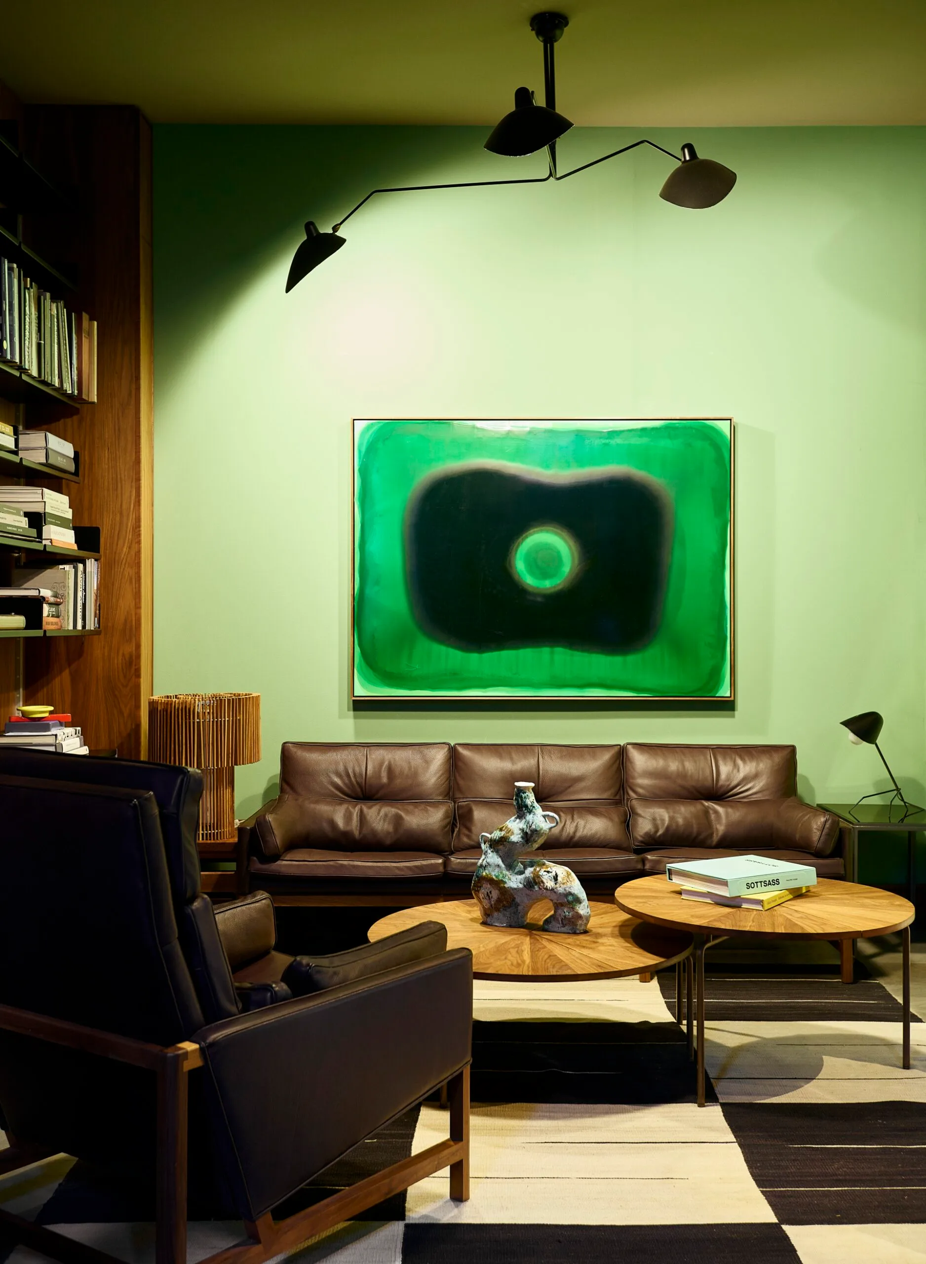 A green sitting room with a black and white rug and round timber coffee tables