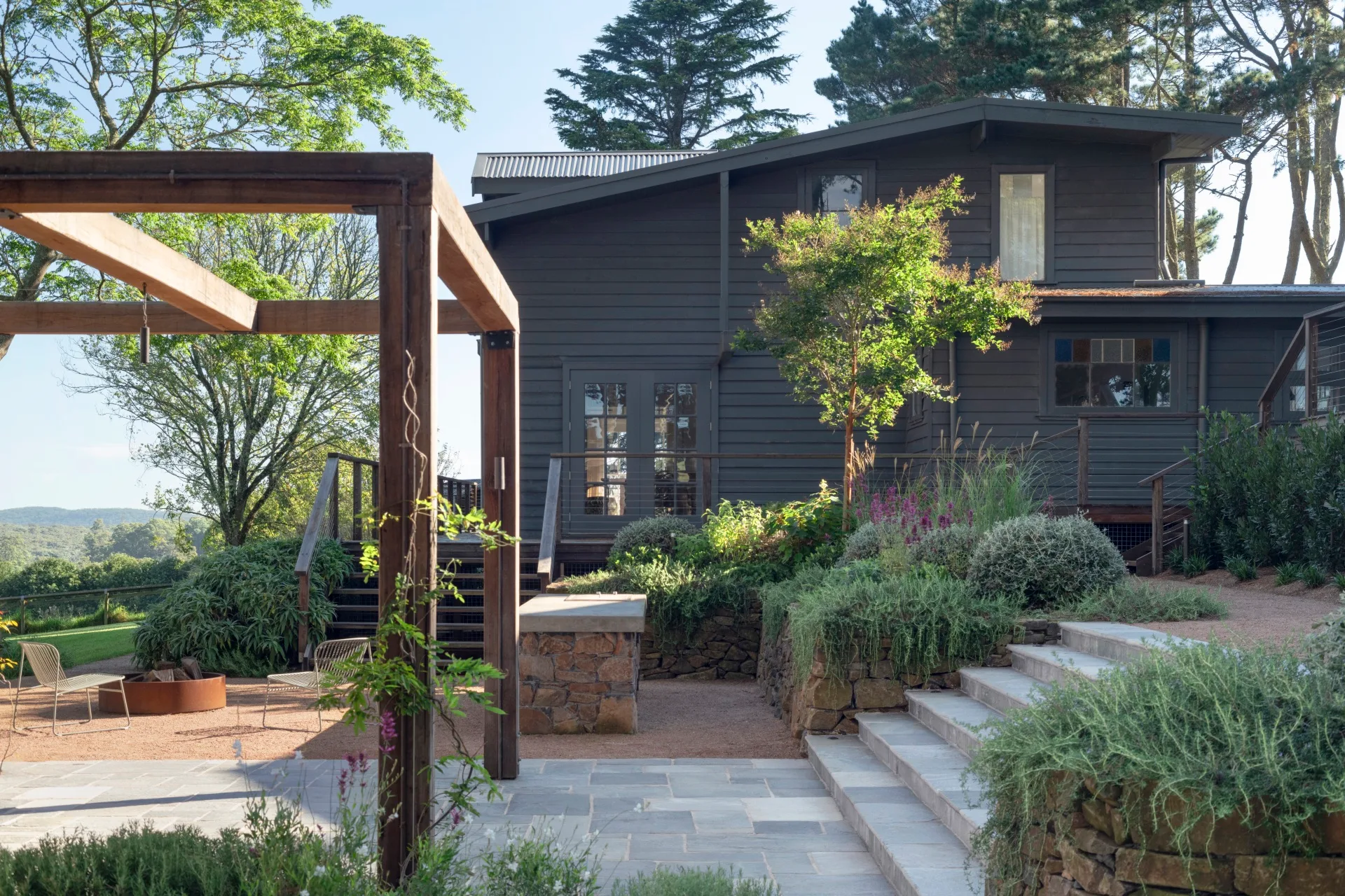 A dark grey weatherboard home beside a pergola and garden beds