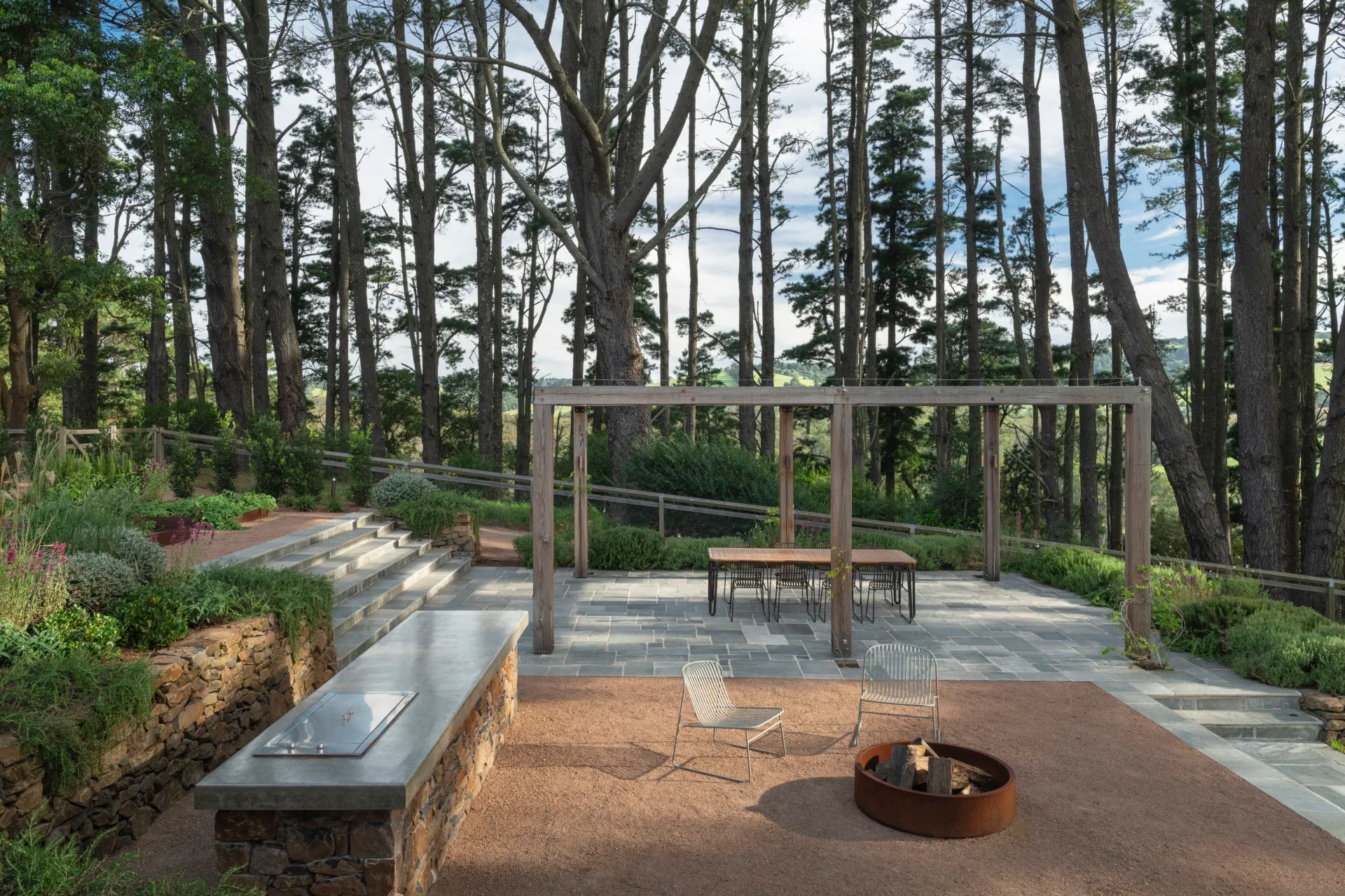 A gravel fire pit and barbeque area surrounded by towering trees