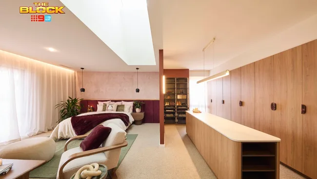 Luxurious bedroom from "The Block" with stylish decor, large bed, closet, and seating area, featuring warm tones and plants.