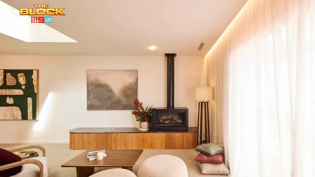 Living room with modern decor, fireplace, abstract art, wooden accents, and soft lighting from large windows.