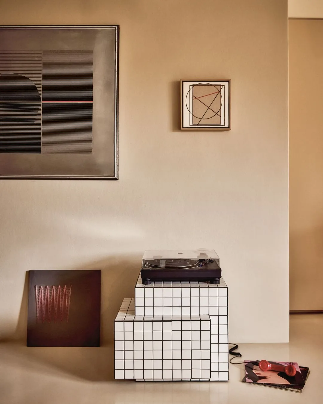 A neutral coloured entrance hall with artworks on the wall and a Technics turntable atop a geometric tiled cube.