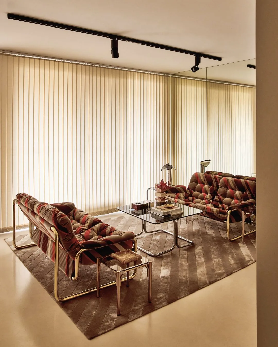 Stylish living room with patterned sofas, glass tables, and tall beige blinds covering large windows.