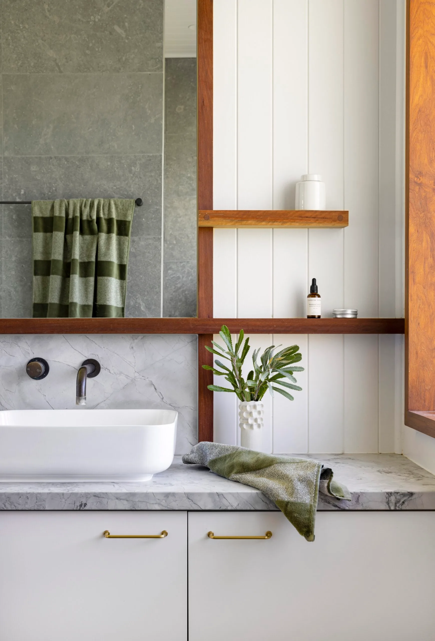 A white bathroom with grey stone benchtops and green handtowels