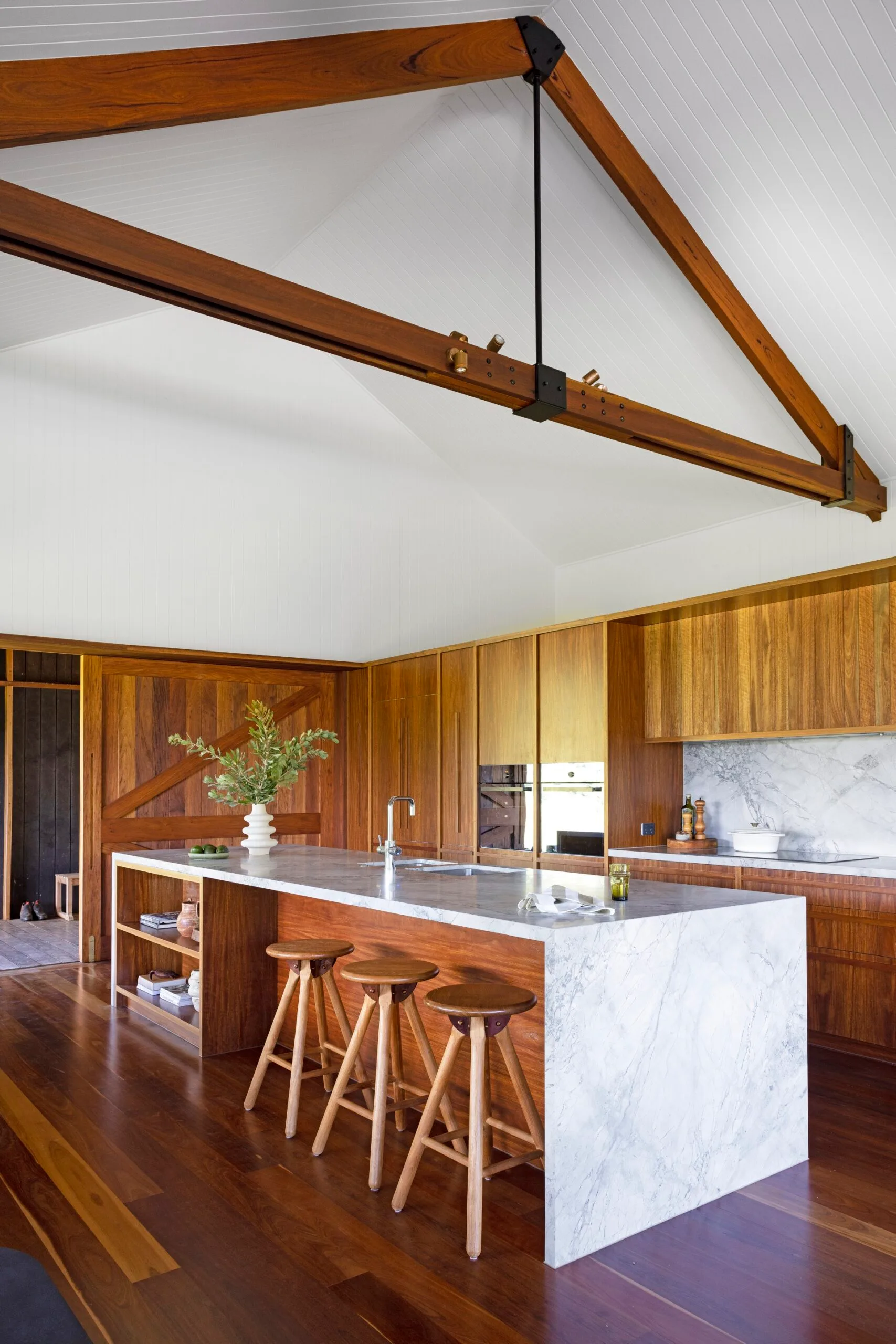 A living room with exposed frame and a timber clad kitchen