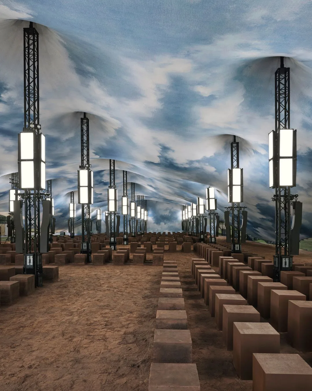 earth-toned seating cubes flank the runway ground inside a tent with a ceiling designed to mimic a blue sky at Burberry SS26. 