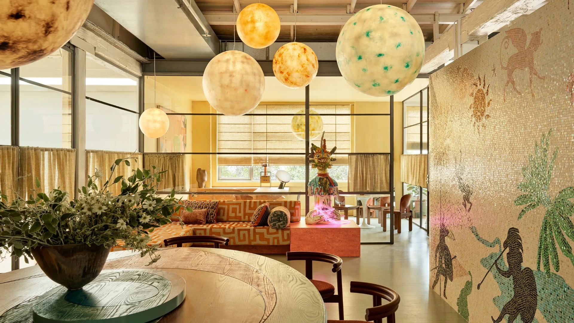 The kitchenette in the Alemais Sydney offices is wrapped in a custom glass mosaic tiled wall with round pendant lights hanging from the ceiling and a large round dining table. 