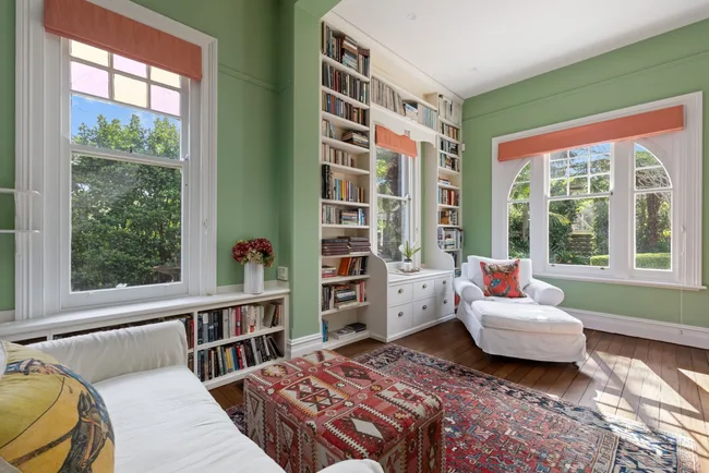 A green sitting room with white sofas and sash windows