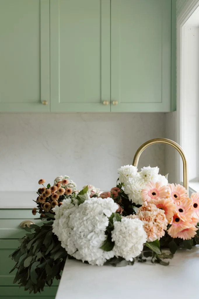 A country kitchen with green cabinetry and fresh flowers