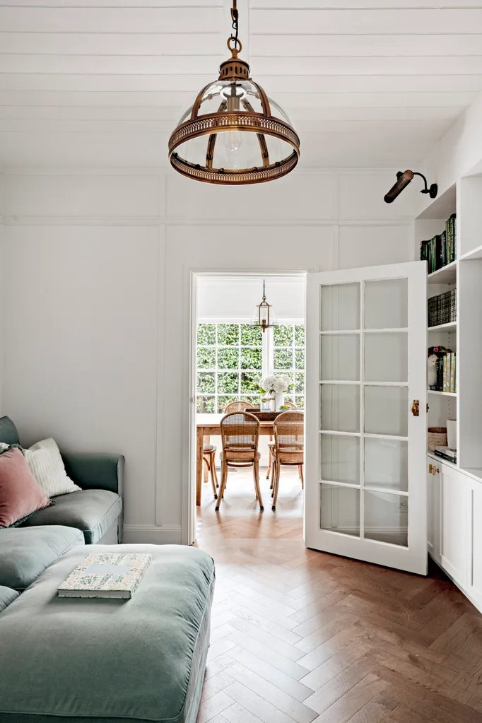 A country home with herringbone flooring, brass lightfittings and a green sofa.