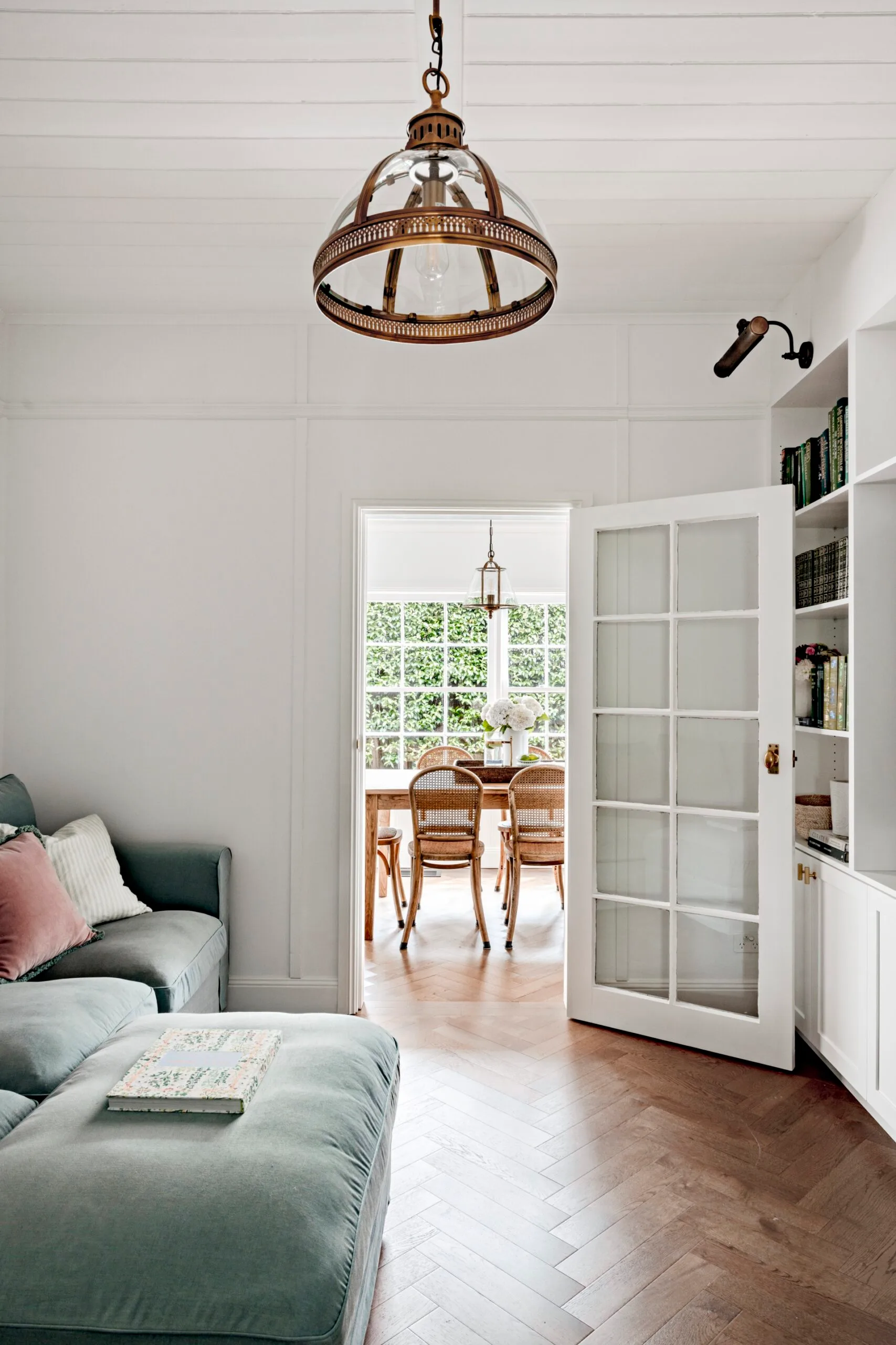 A country home with herringbone flooring, brass lightfittings and a green sofa.