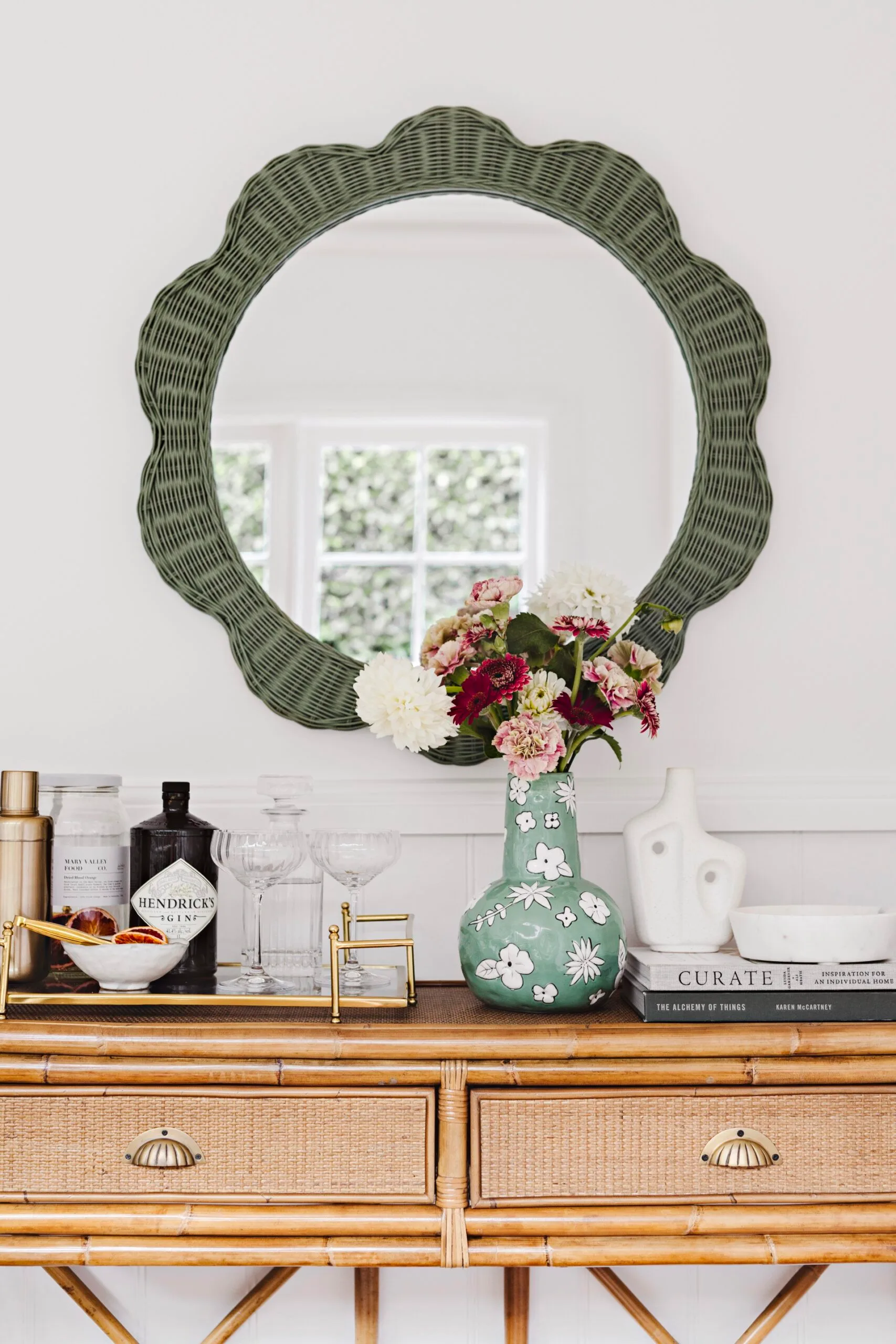 Green wicker mirror and cookbooks adorn a sidetable.