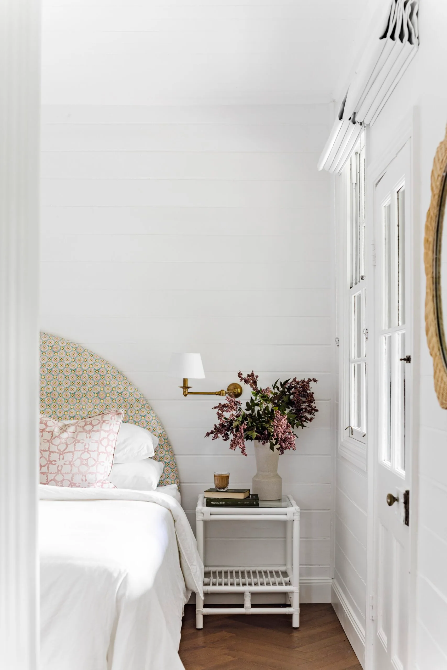 All-white bedroom with wicker furniture and soft, colourful fabrics.