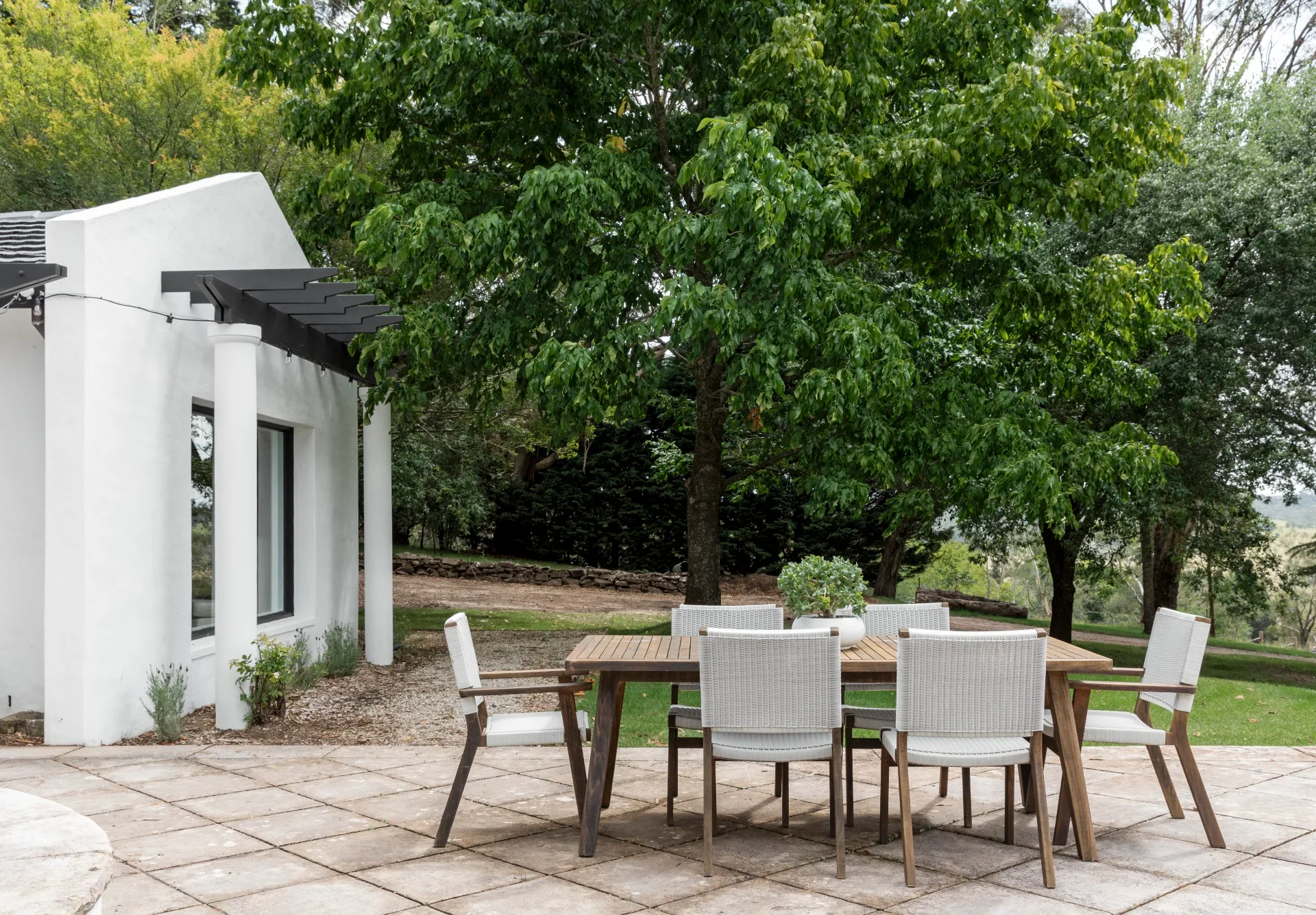 An alfresco dining area with a timber dining setting beside a white house