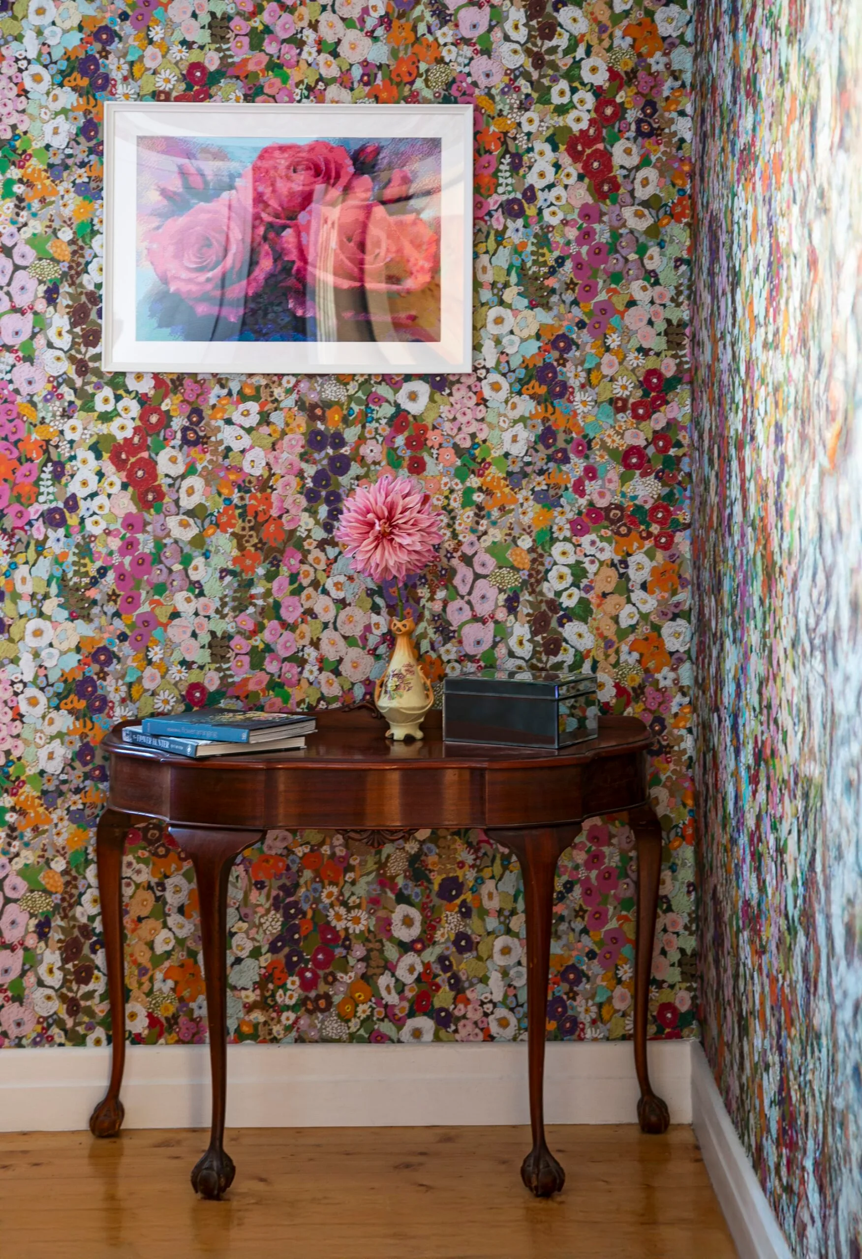 Floral wallpaper in spring shades above a vintage side table.