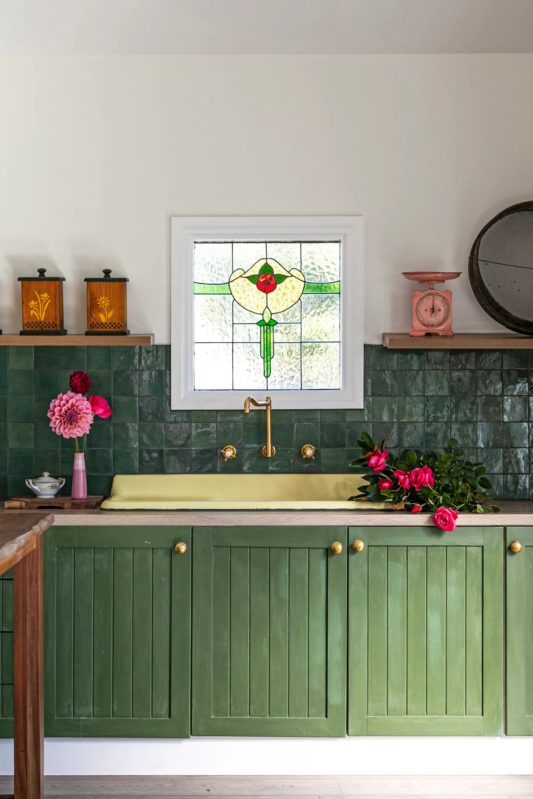 A stained glass window in a green kitchen decorates with vibrant pink flowers.