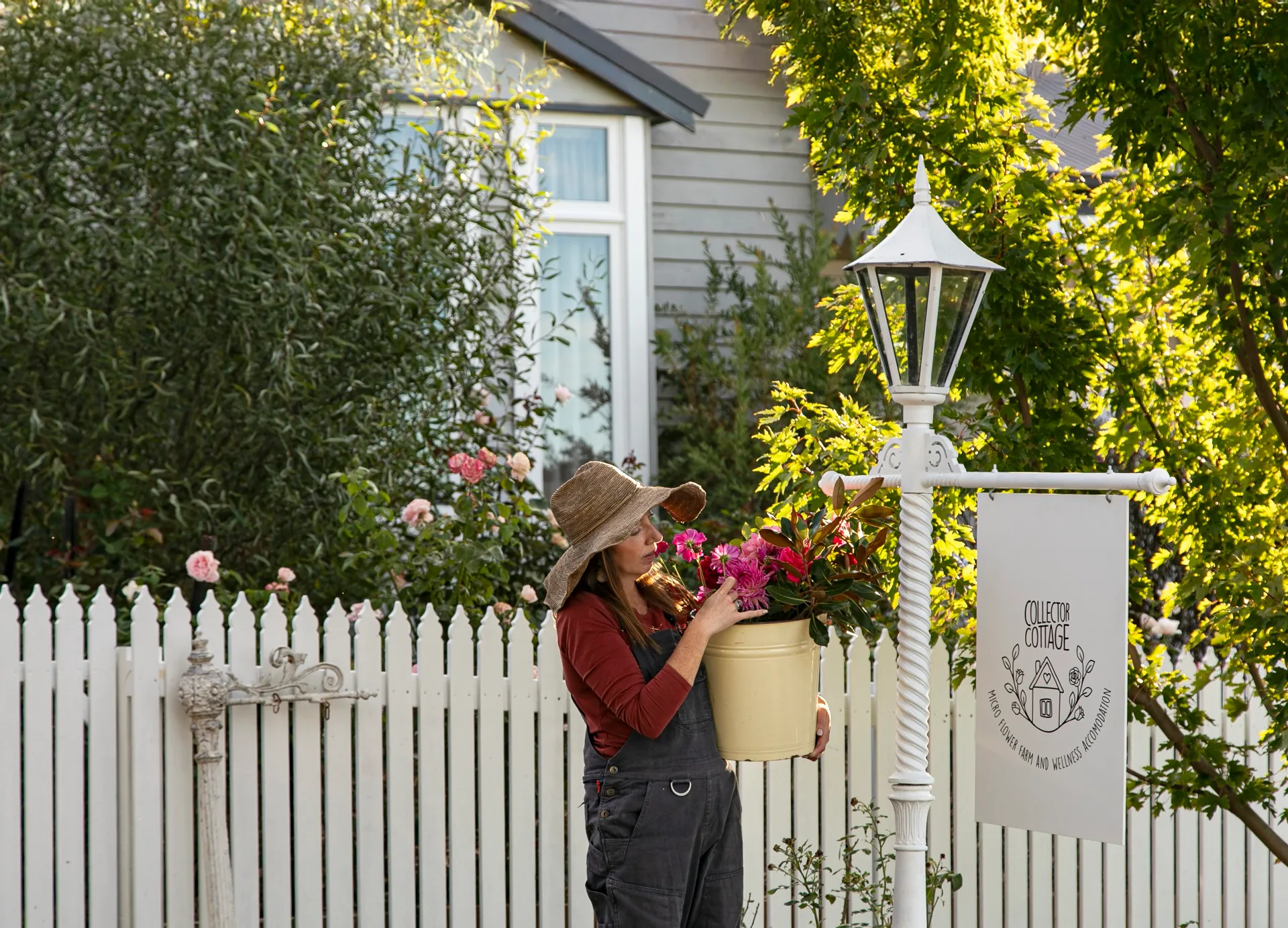 A woman in front of a white picket fence with a bunch of vibrant pink flowers.