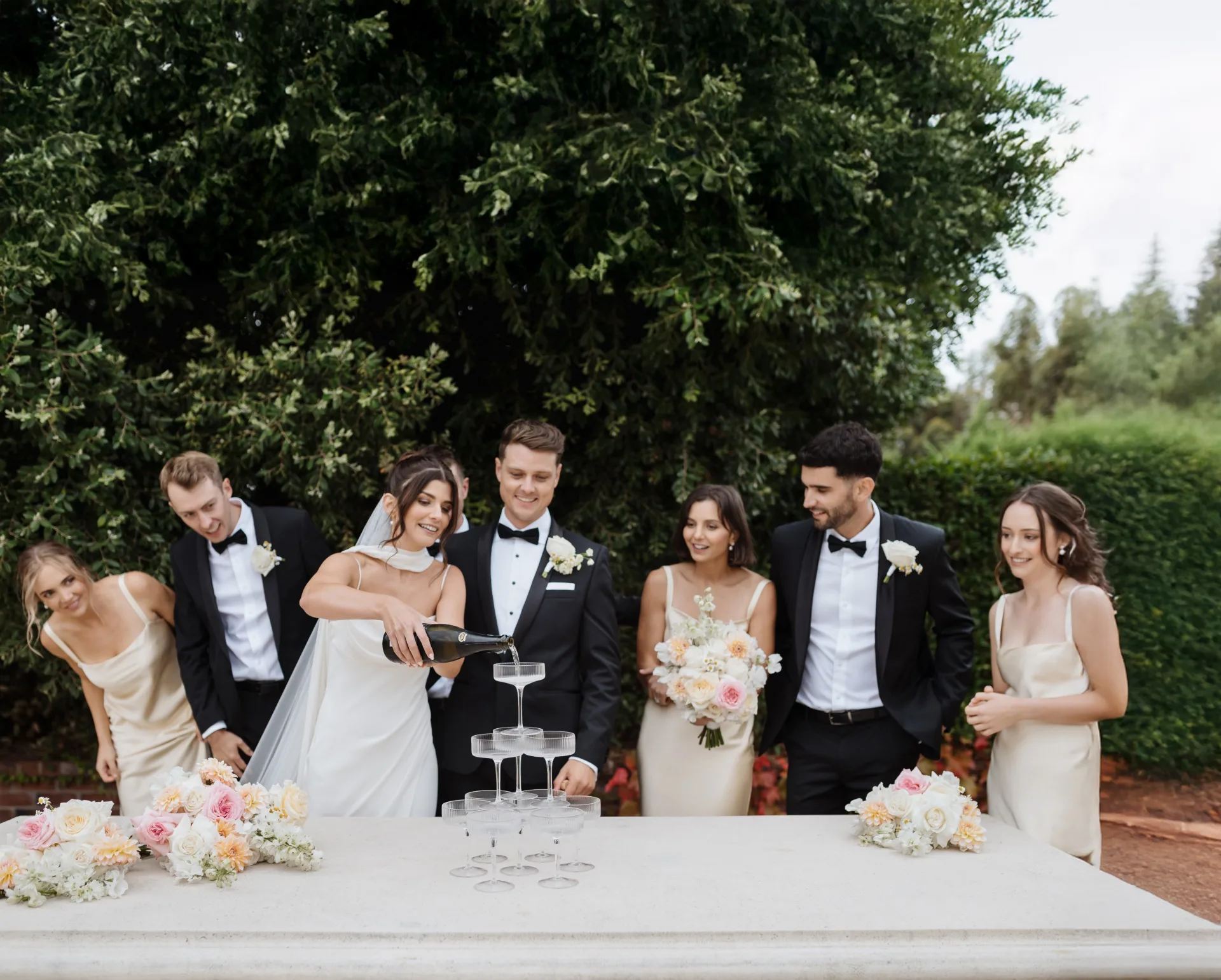 A bride pours a champagne tower with her husband and bridal party