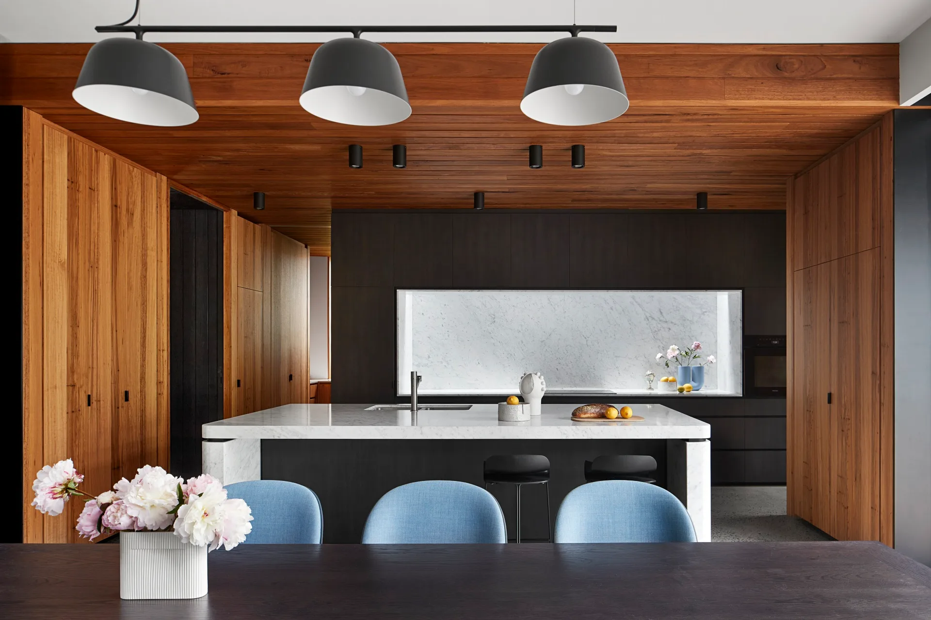 Modern kitchen with warm wood ceiling and blue dining chairs. Belle