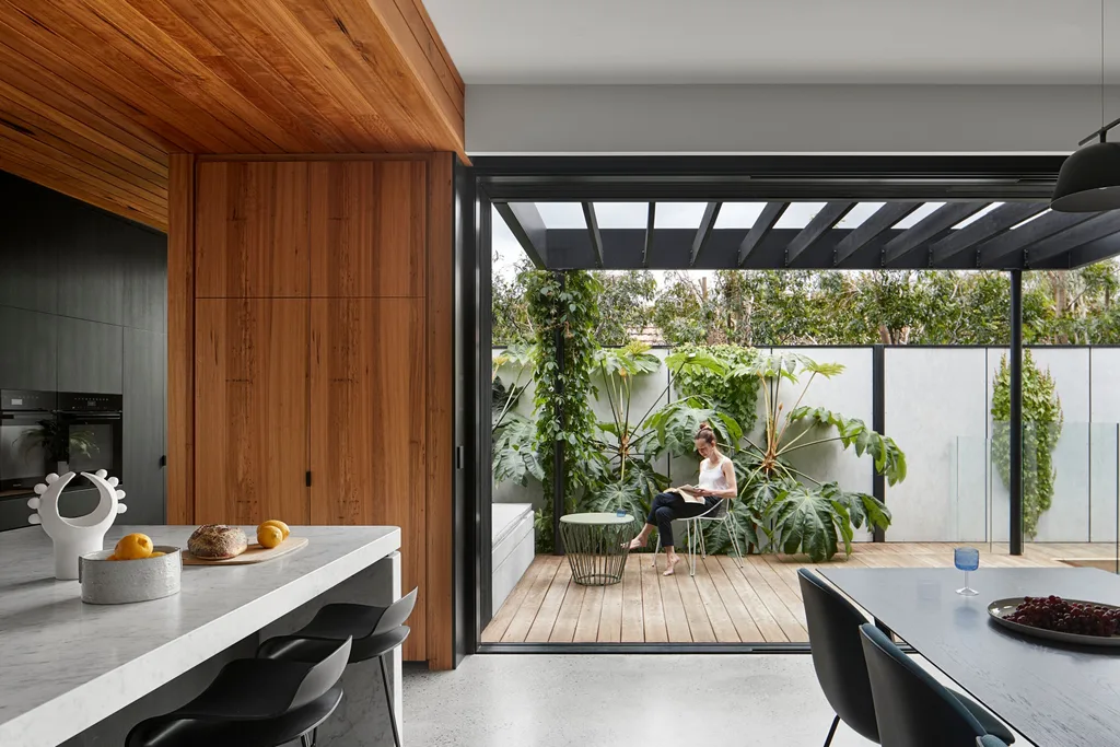 Woman sitting on deck with lush greenery and modern kitchen. Belle