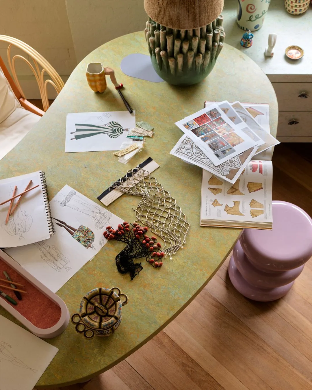 Overhead shot of the green, curved desk at Alemais Sydney offices, covered in fashion illustrations of future collections. 