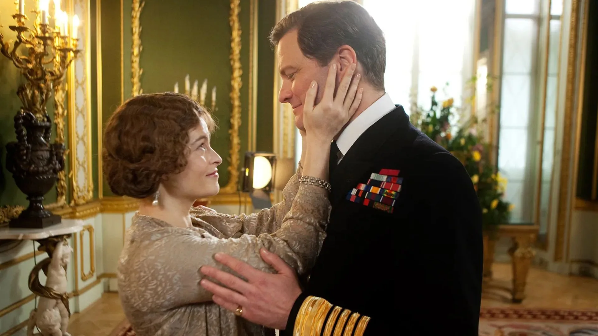 A woman clasping the face of a man lovingly in an ornate stately home. 