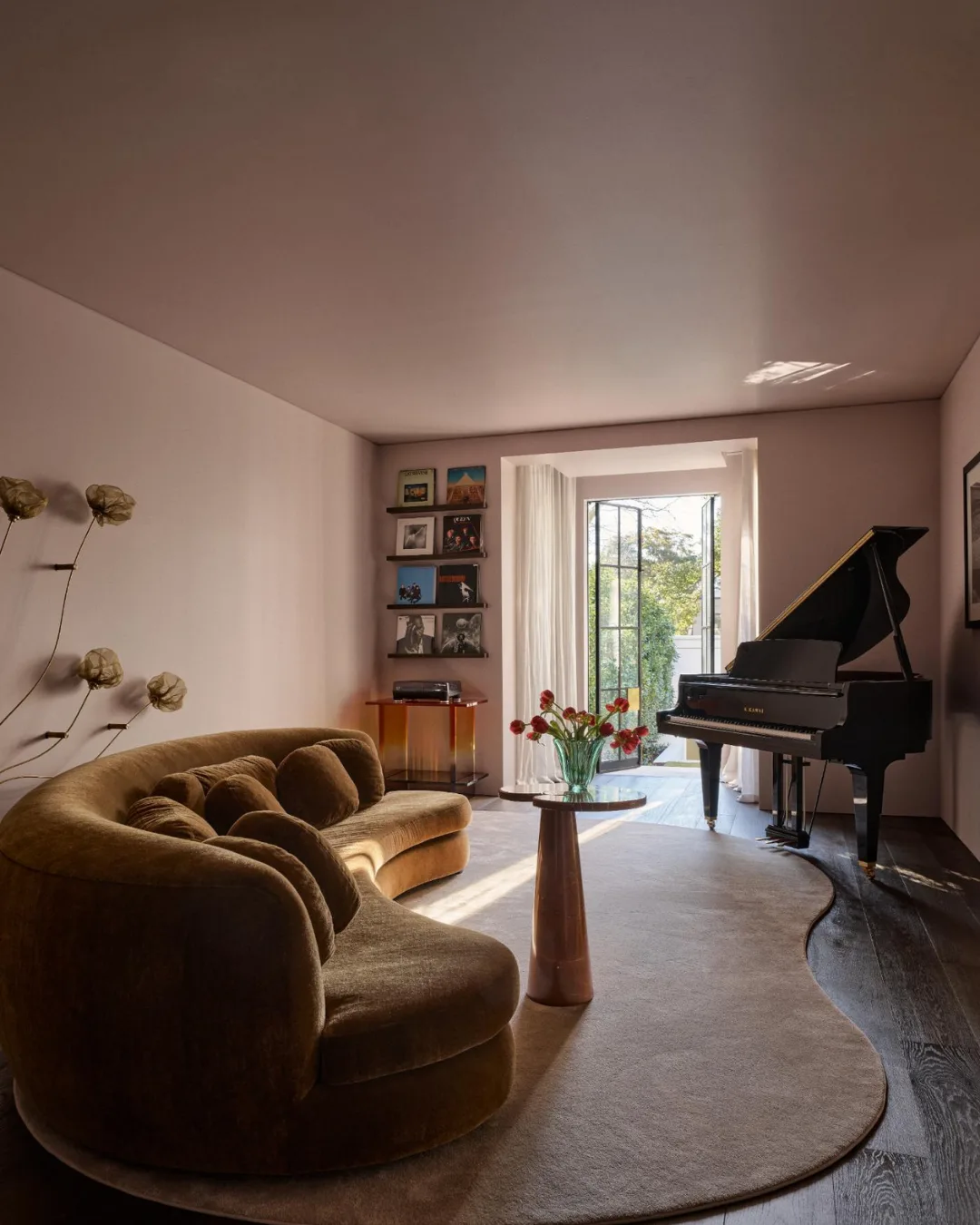 Curved brown sofa near a grand piano, with flowers on a small table in a sunlit room.