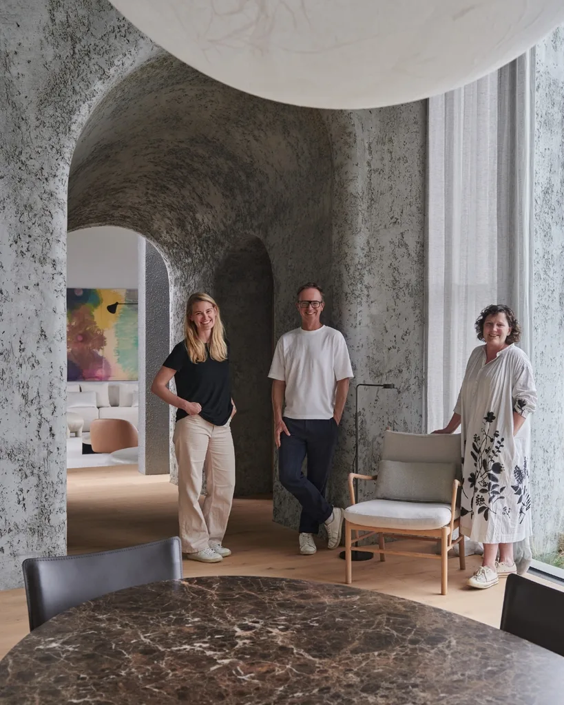 Three people pose in a modern room with textured walls and a marble table.