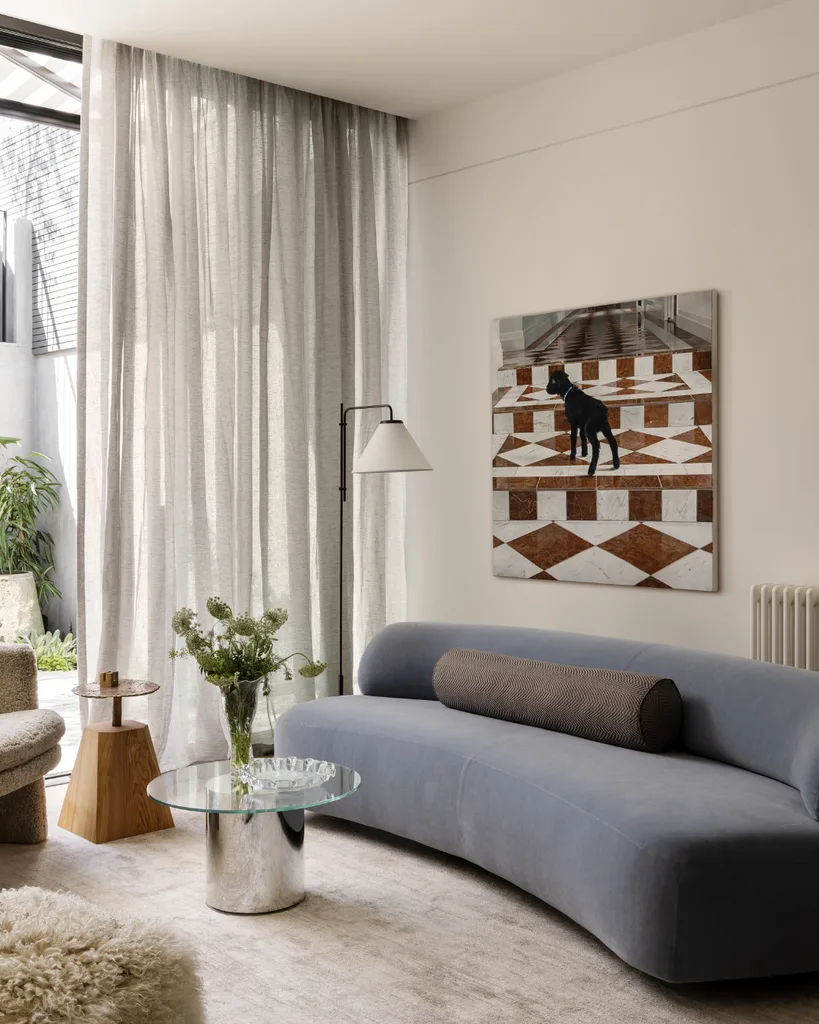 Contemporary living room with a curved sofa, abstract art, and a large window with sheer curtains. Mim Design verdant residence.