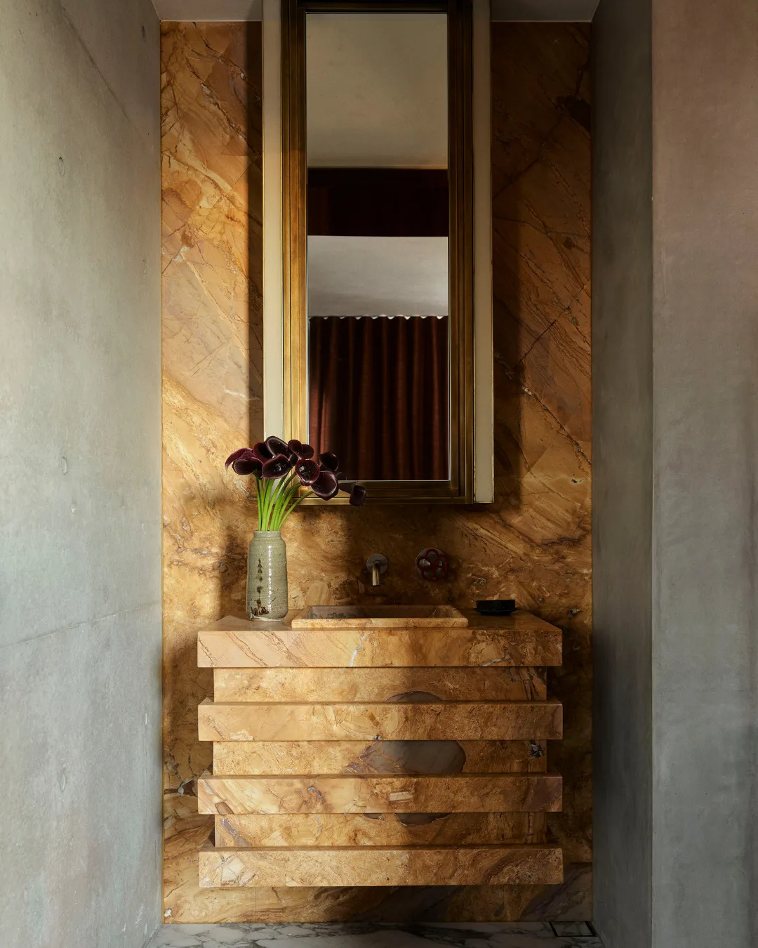 Brown marble powder room with floating basin and tulips in a ceramic vase.