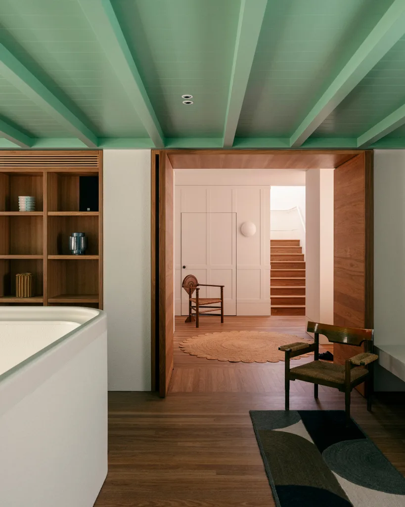 Modern interior with green ceiling, wooden floor, and furniture. Open door reveals a corridor and staircase in the background. Belle interior design awards Richards Stanisich.