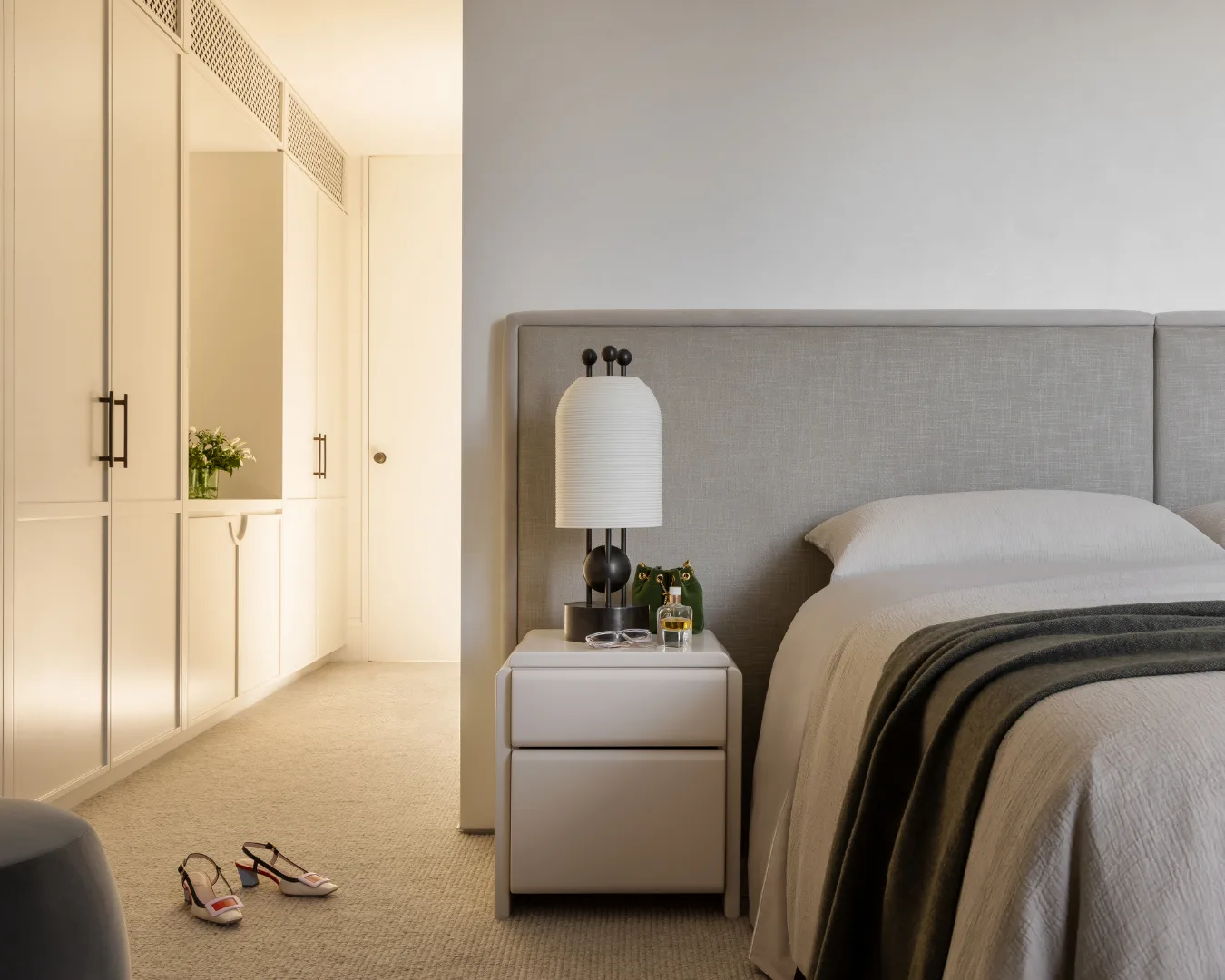 A modern bedroom with a neatly made bed, a nightstand, and a pair of shoes on the carpeted floor. Mim Design verdant residence.