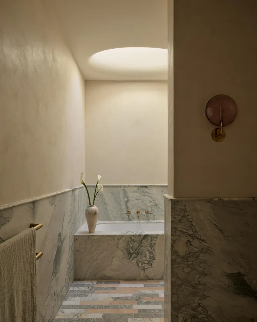Luxurious bathroom with marble tub, vase with flowers, and soft lighting from a circular skylight.