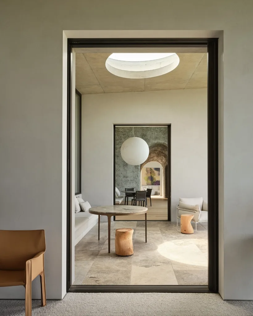 Modern interior with circular skylight, minimalist furniture, and neutral tones, featuring wood stools and a round table.