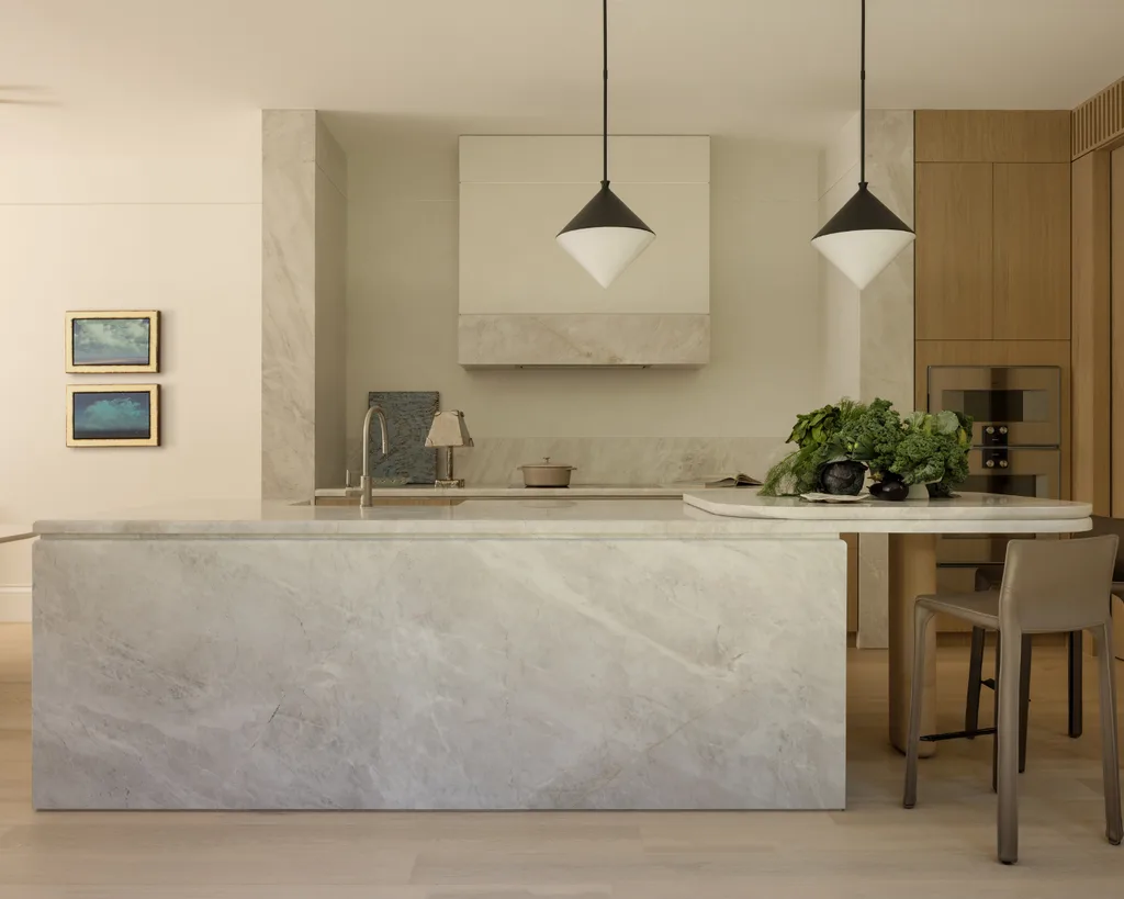 Luxurious modern kitchen with marble island, pendant lights, wall art, and fresh greens on the counter. Mim Design verdant residence