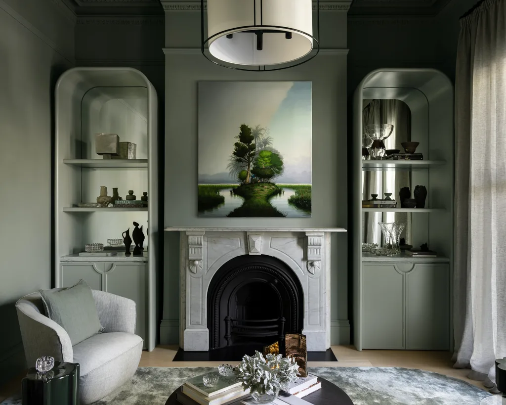 Sophisticated living room with a marble fireplace, artwork, built-in shelves, and soft green-gray walls. Mim Design verdant residence.