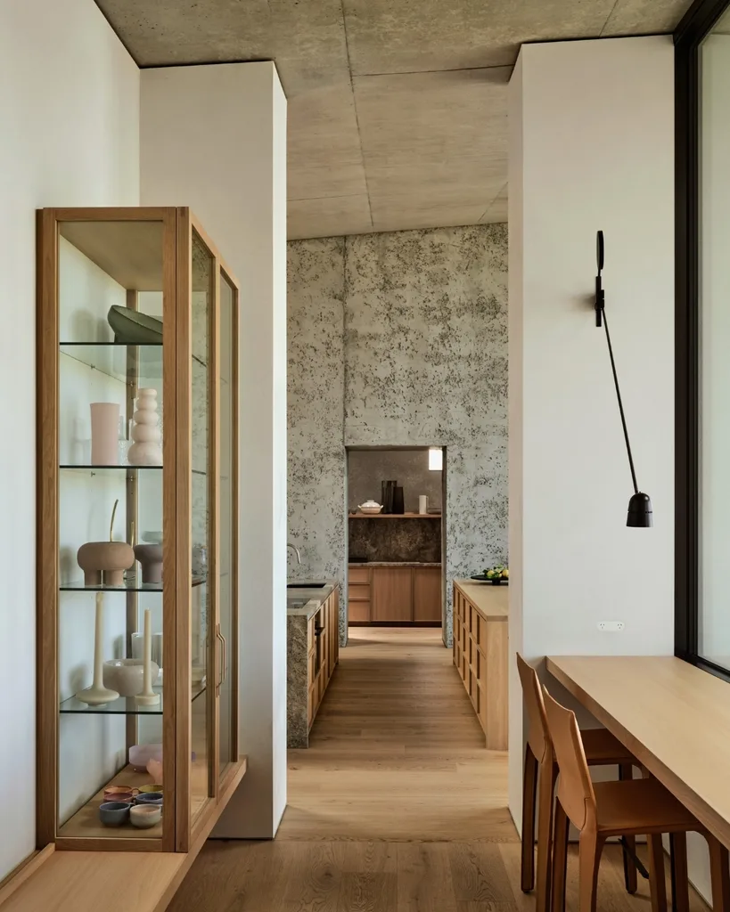 Modern kitchen with wooden floors, minimalist decor, glass cabinet, and dining area with two brown chairs. |