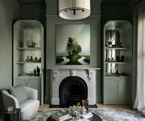 Sophisticated living room with a marble fireplace, artwork, built-in shelves, and soft green-gray walls.