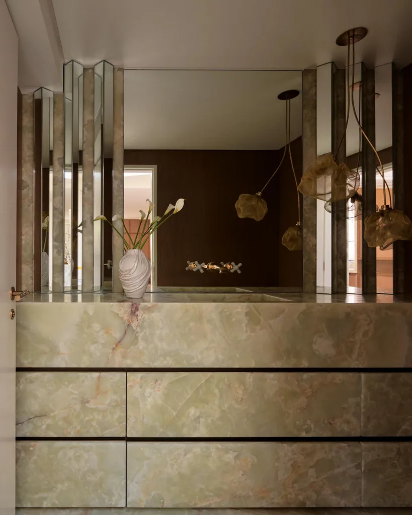 Green marble console with a white vase and flowers, mirrored accents, and hanging pendant lights in a modern interior.