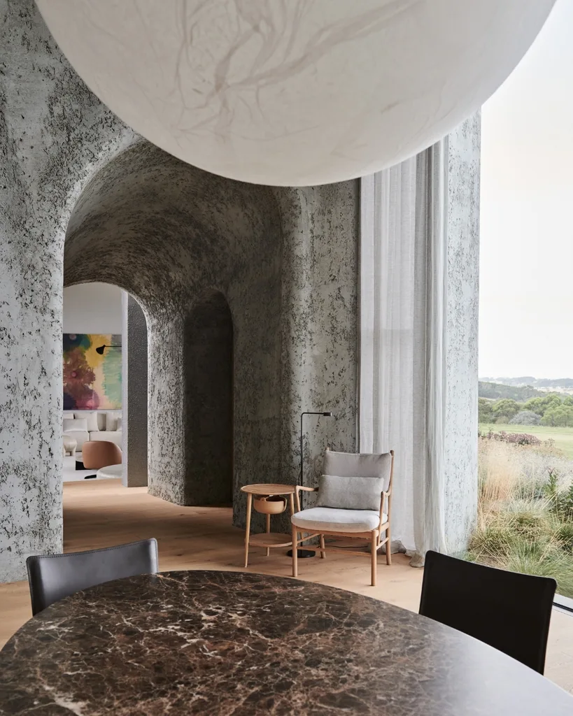 Marbled round table with black chairs near textured archway, modern chair, and window with outdoor view. |