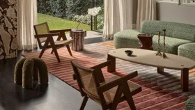 Cosy living room with mid-century furniture, patterned rug, and large windows overlooking a green garden.
