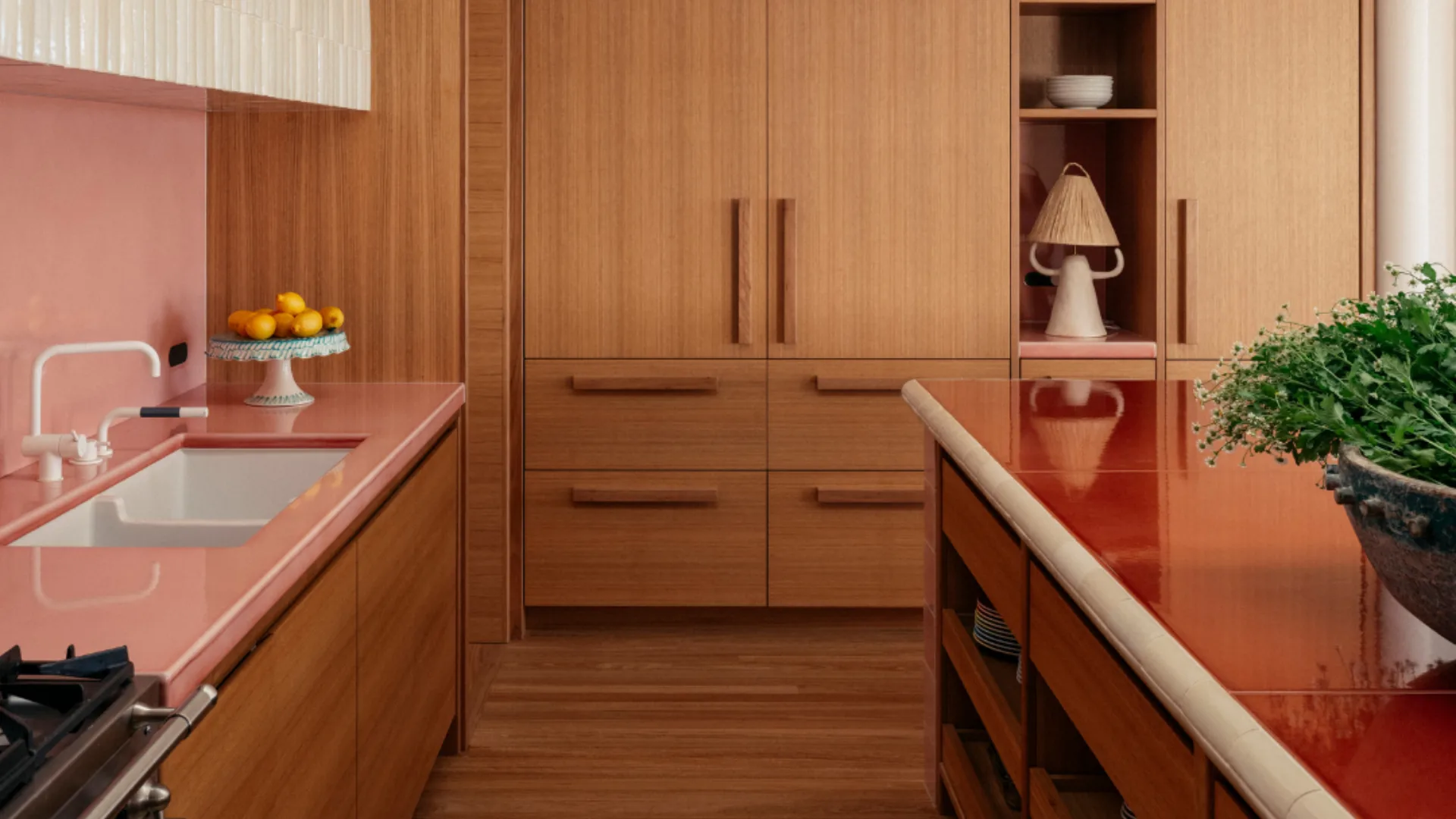 A modern kitchen with wood cabinets, red countertops, a potted plant, hanging woven lamp, and a bowl of lemons.