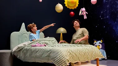 A child sitting in a bed with a Bluey x Koala headboard