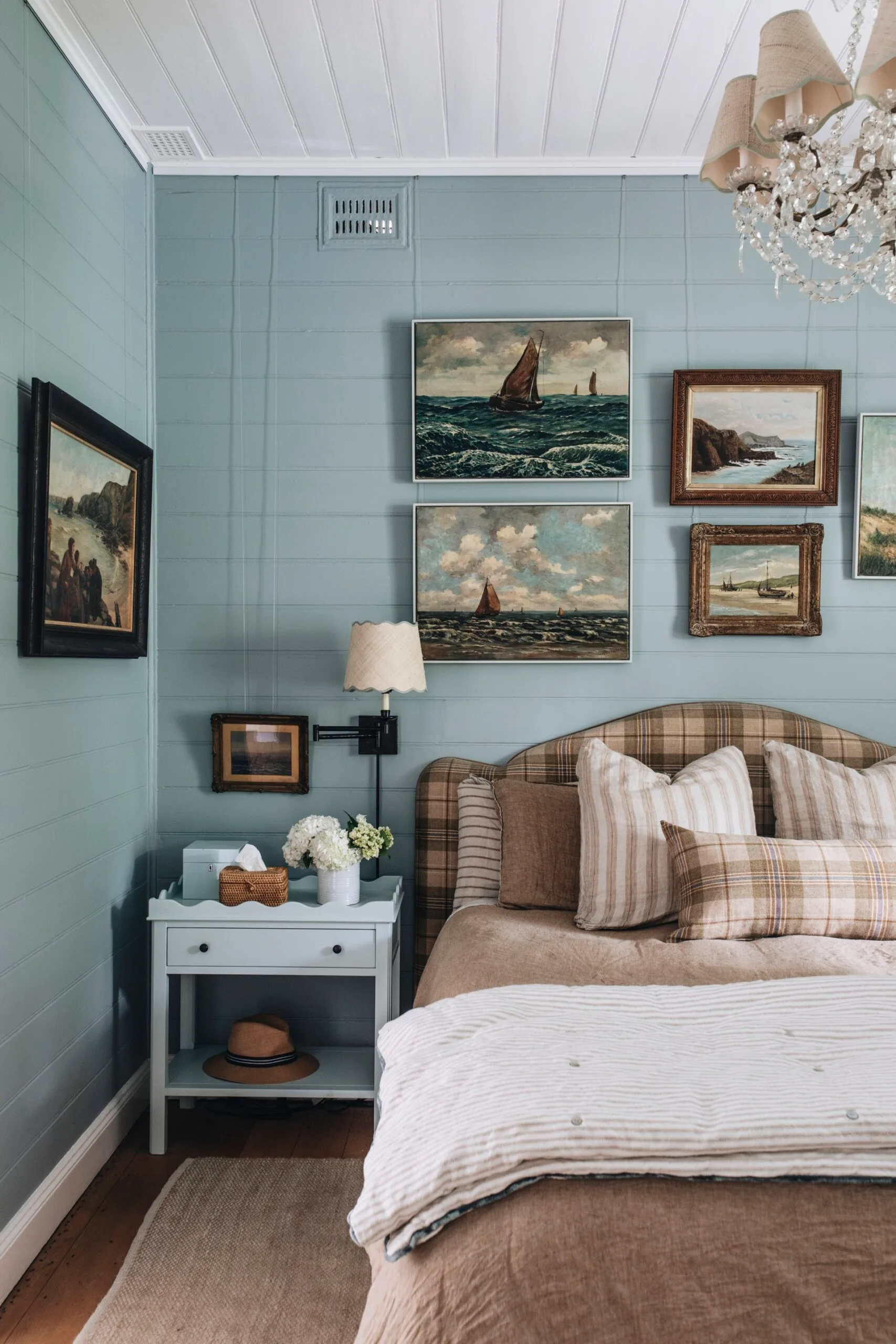 A blue bedroom with a gallery wall and plaid headboard