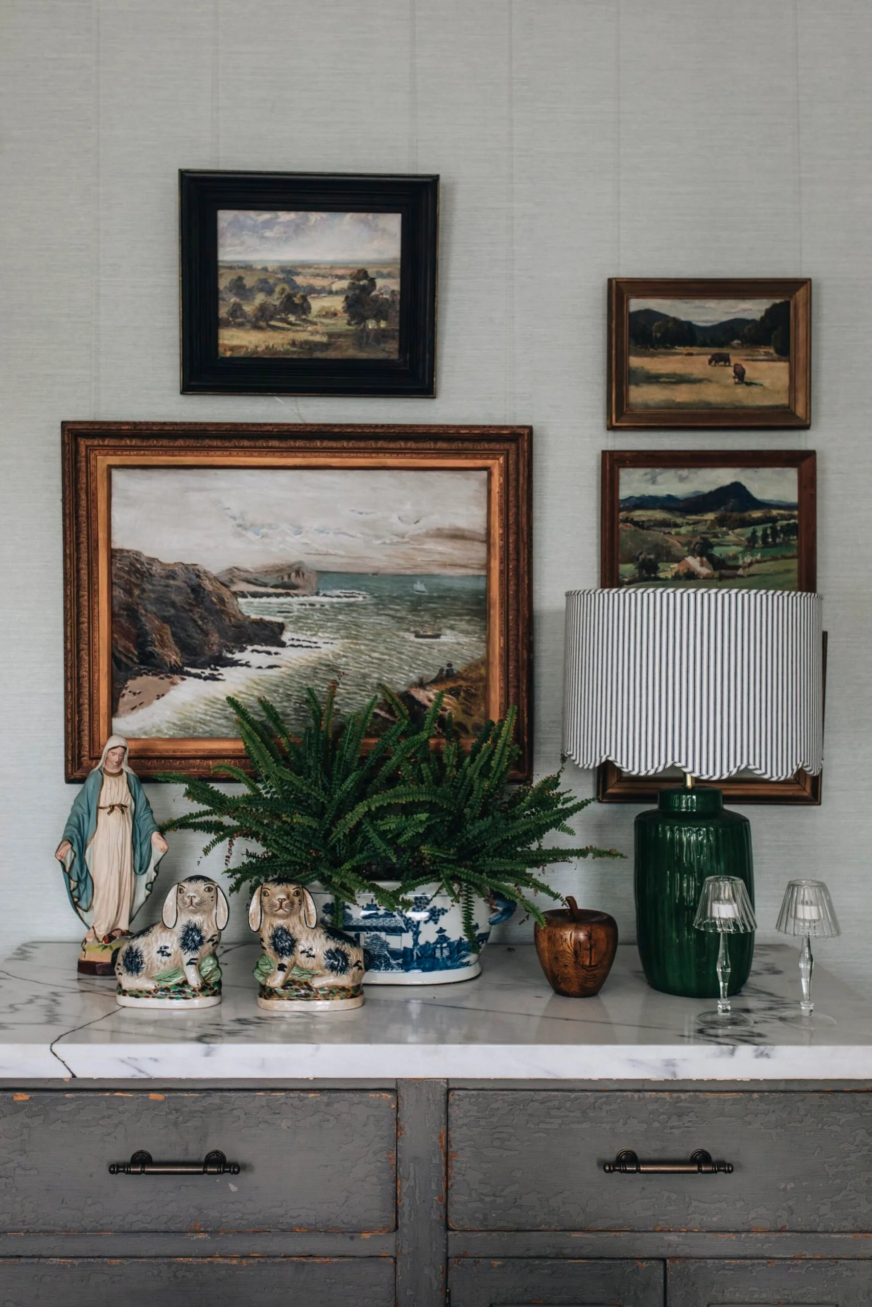 A side table with ceramics and framed paintings hanging above