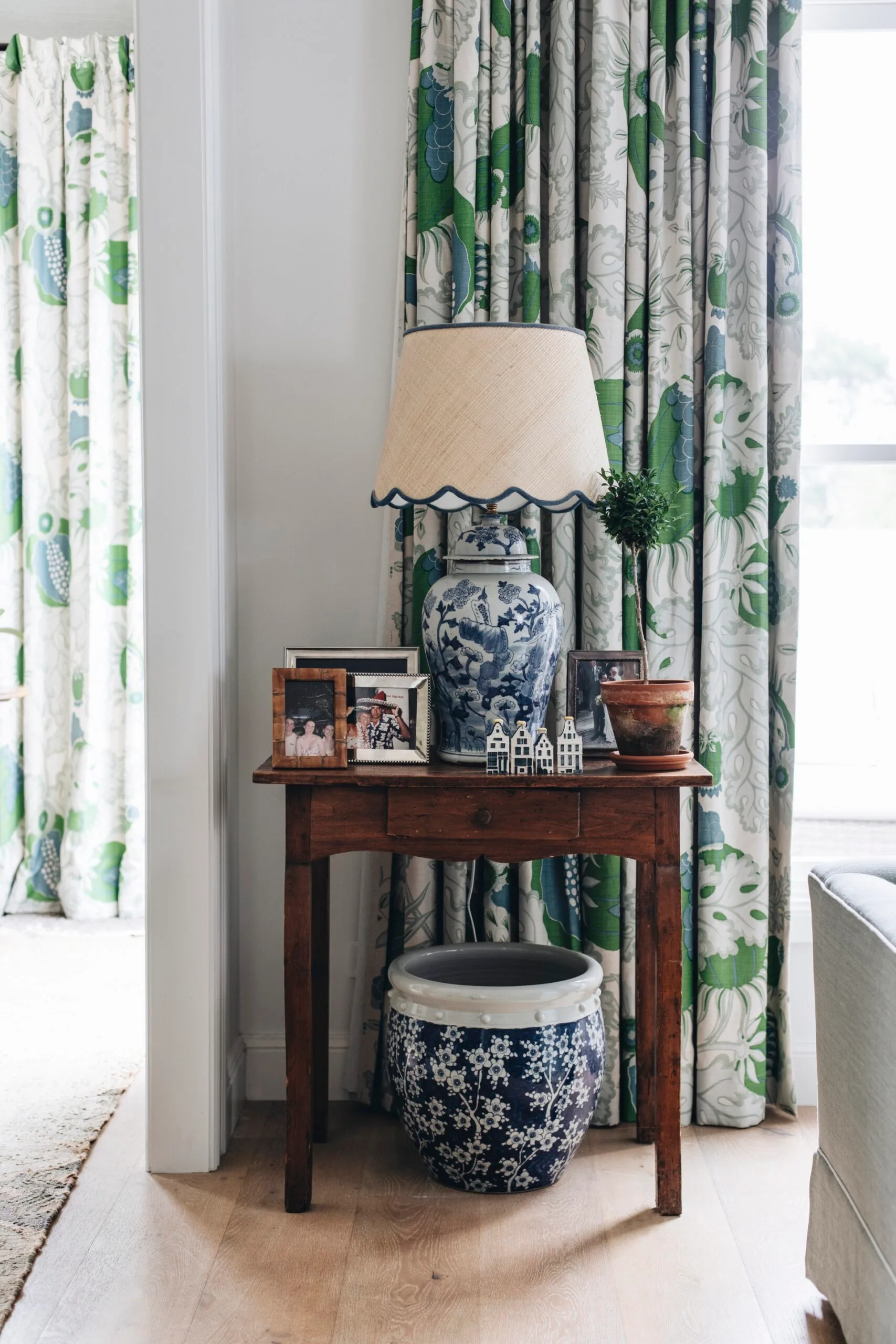 A side table with a large ceramic lamp and framed family photos