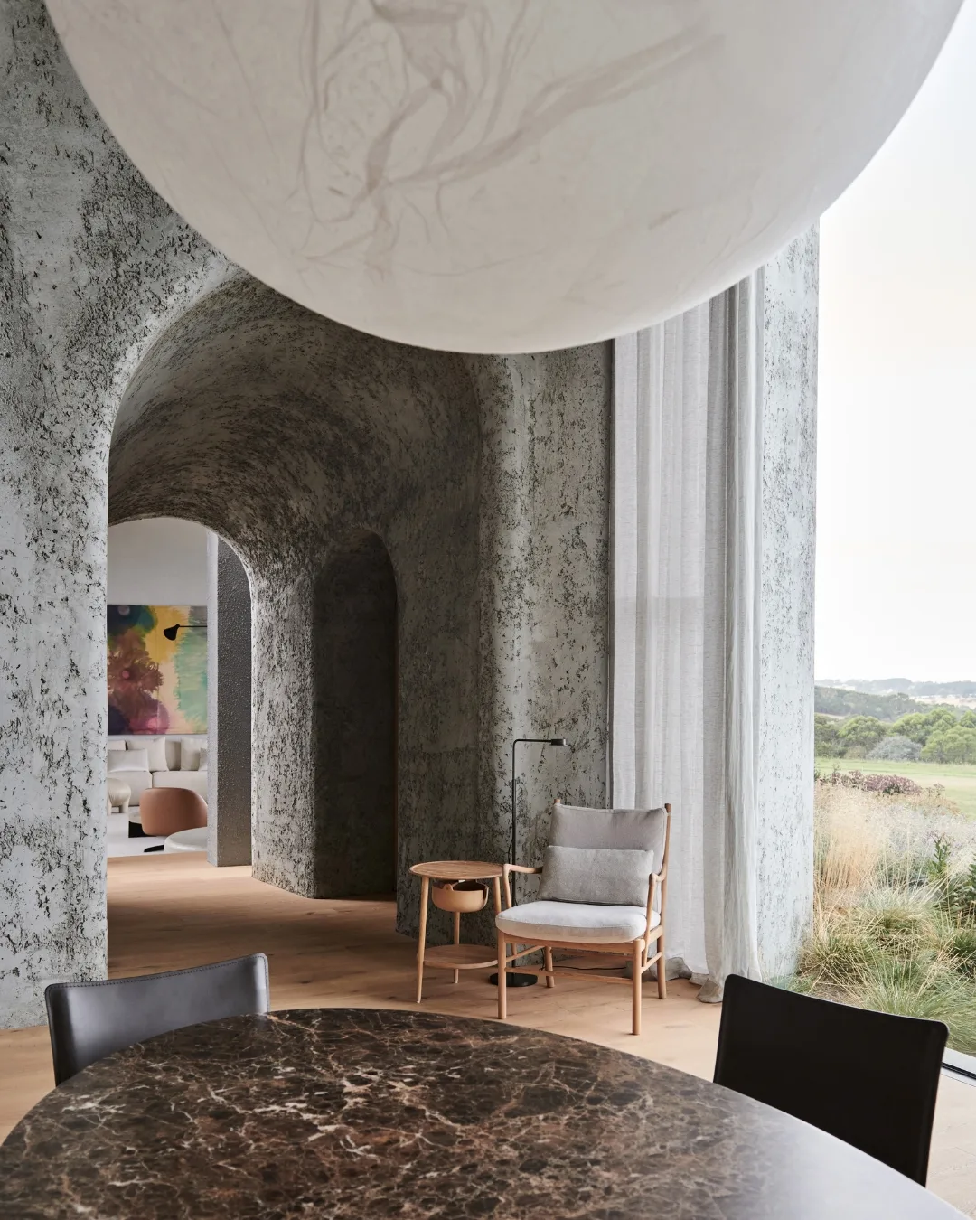 Concrete arched hallway with marble dining table, white lantern, sheer curtains in front of windows.